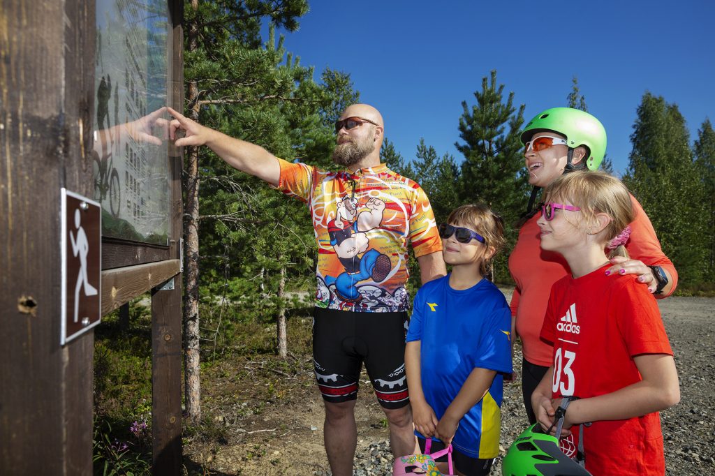 Nelihenkinen perhe opastaulun ääressä lähdössä maastopyöräilemään.