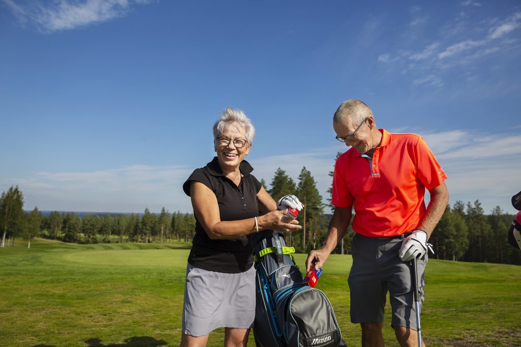 Keski-ikäinen pariskunta golfkentällä mailakassin kanssa kesäpäivänä.
